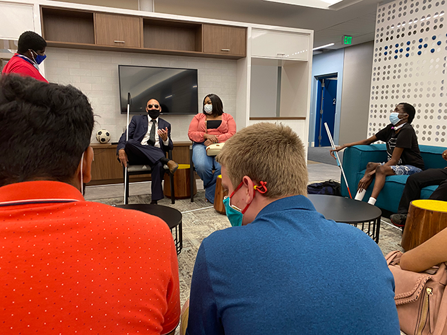 A blind professional in a blue suit with a white cane speaks to blind students.