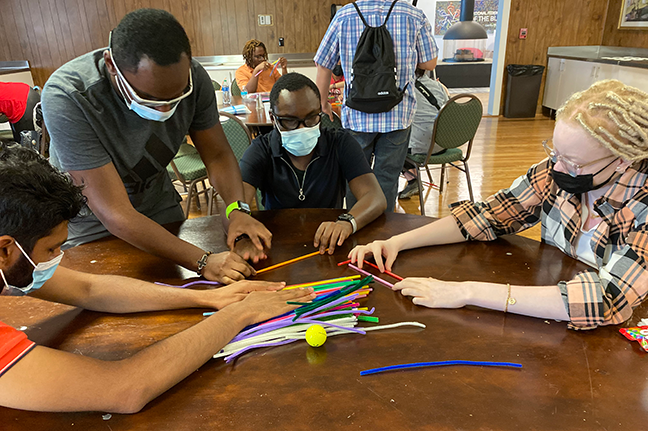 Four blind students at a round table, touch materials for a team building activity.