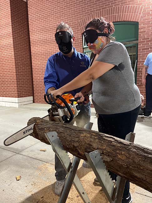 NFB staff member, Danielle McCann is halfway through the log with the chainsaw. President Riccobono helps from the side.