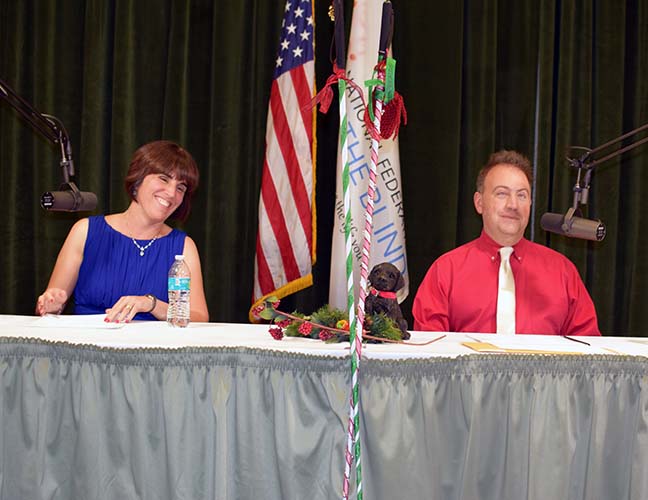 Pam Allen and Mark Riccobono smile together on stage a pair of decorated canes lean in front of the table between them.
