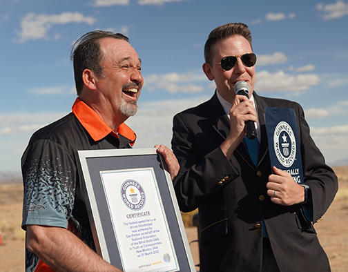 Dan Parker smiles widely as he accepts his Guinness World Record certificate from the GWR Official.