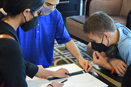 Two mentors and an EQ participant (Pierluca) using a Braille ruler to measure foam core board, which they will then cut to form the walls of their model house.