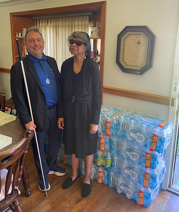 Mark Riccobono and Jackson Chapter member Barbara Hadnott stand in her home in front of a stack of donated bottled water.