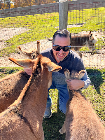 Kevin McNally smiles while cuddling with some donkeys.