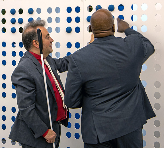 Jason Broughton takes a turn at writing a Braille message by moving the tennis balls as Mark Riccobono advises.