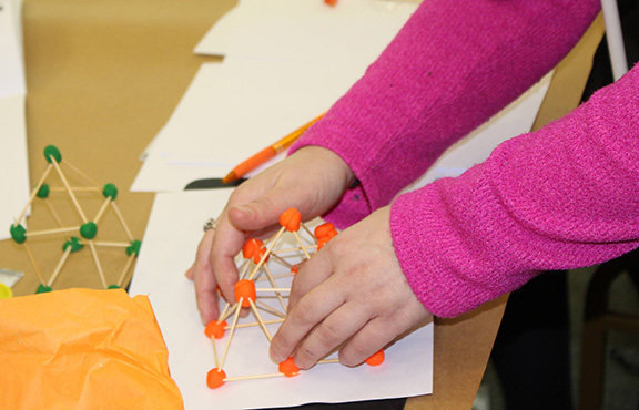 Hands building a geometric moon base made of toothpicks and playdough. 