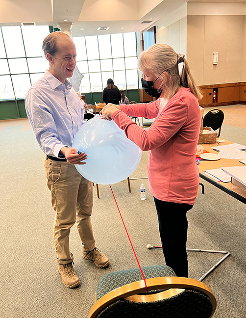 Teachers Justin Harford and Jenny Carmack work with a balloon and string (the string is attached to a chair). The point is to show how a rocket works given action and reaction.