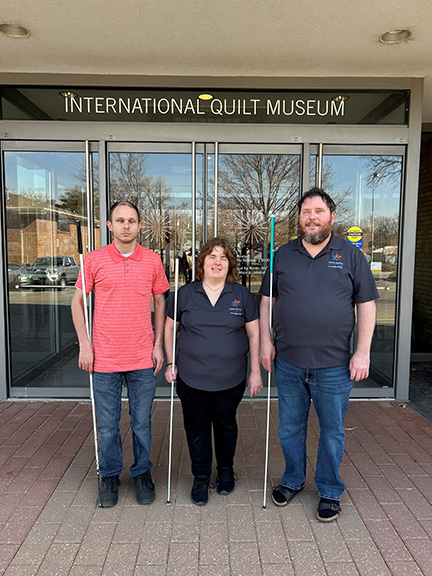 Jeremy Fifield, Amy and Shane Buresh holding their long white canes outside the International Quilt Museum.
