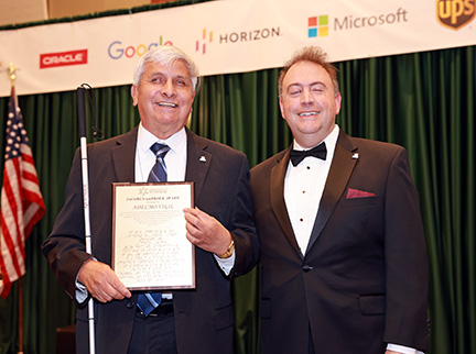 Adelmo Vigil holds his plaque with Mark Riccobono smiling beside him.