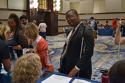 Many members signed up to attend the career fair at convention. Here, NFB of Texas member Derick, looking sharp in his suit, speaks with a potential employer.
