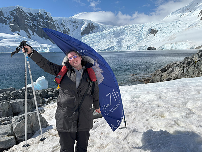 Erin Daley smiles on the Seventh Continent. Snow mountains and the ocean can be seen behind her.