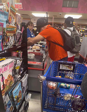 Two students place items onto the checkout counter at a grocery store.