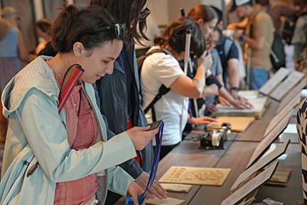 At the Museum of the Blind People&rsquo;s Movement display, Emeline examines a Six Dot Dash medal from the NFB of Colorado. This medal was given to participants of the National Federation of the Blind of Colorado&rsquo;s 6 Dot Dash in 2024, an annual 5k race that supports Braille literacy for blind children, blindness skills training, and more.