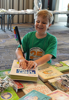 Emerson smiles widely while reading the cover of a Braille book.