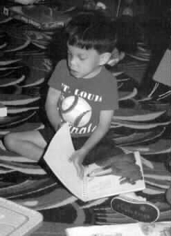 Photograph of a five or six-year-old boy seated on the floor, reading a book, and