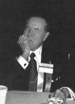 Dr. Jernigan sits at a table listening to a speaker