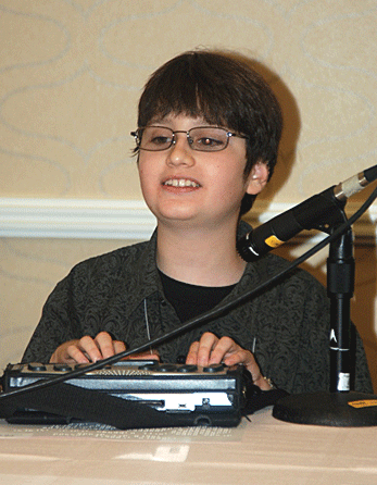 With his hands on his Braille notetaker, a preteen speaks into a microphone.