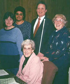 NFB President, Marc Maurer, stops for a chat with busy Readers Are Leaders volunteers.   On the left are NFB members Bernice Lowder and Mary Kuforiji, and on the right are Rolling Hills Federated Women's Club members Katherine Carbonneau and Aline Norris.