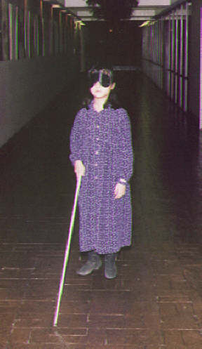 This youngster wears sleepshades as she practices her cane travel skills in a long corridor.
