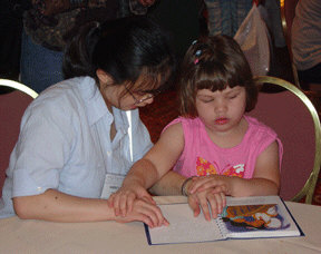 A former Braille Readers Are Leaders winner, Harriett Go (Pennsylvania), demonstrates two-handed Braille reading to novice reader, Melissa Davis (Geogia).