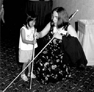 Blind roll models are important to young cane users.   The Cane Walk, Youth Scavanger Hunt, and Braillew Carnival at the 2000 convention provided many role modelong opportunities.   In the photo, Sheila Koenig gives some gentle hand-underr-hand cane instruction to Winona Brackettt at the Braille Carnival.
