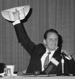Marc Maurer waving a cowboy hat on the podium at the 1993 NFB Convention in Texas. 