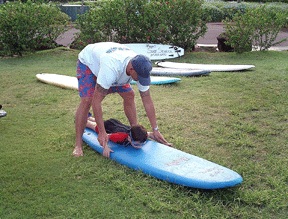 Persistence does pay off as Vejas lies on a surfboard while his instructor, Miguel, teaches him the basics of surfing.