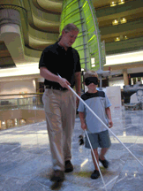 Here instructor Darick Williamson of Louisiana walks with a young boy under sleep shades to demonstrate that even without residual vision, the cane is the ultimate tool for travel in any environment.