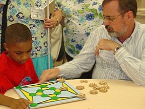 Matt Maurer (IN) explains the rules of this tactile-Braille adapted game to student, Jasani Whitehead, at the 2006 Braille Carnival at the NFB convention.