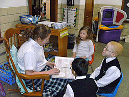 An older student models good Braille skills by reading to three younger students.