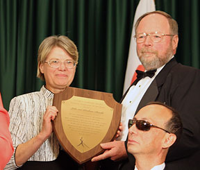 At the convention banquet Barbara and John Cheadle stand on the platform holding their Jacobus tenBroek Award plaque.
