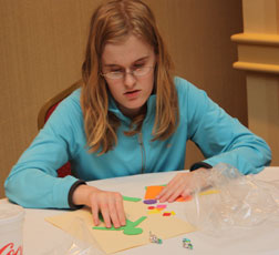Abby Cochran creates a picture by adding colorful shapes to the figure of a man on her paper.