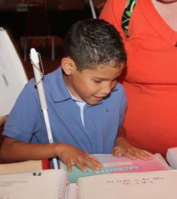 A young boy examines the selection of Braille books on a table.