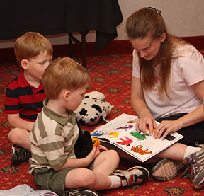 A child care worker at Kids Kamp reads to children from a print/Braille picture book.