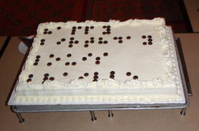A giant sheet cake displays the words HAPPY BIRTHDAY LOUIS BRAILLE written in chocolate dots.