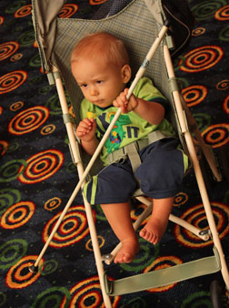 Toddler Brock Kaiser sits in his stroller, holding his 24-inch NFB cane.