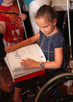 Seated in a wheelchair, Gabby Nicholas of Indiana beams as she holds three Braille books on her lap.