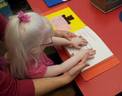 Teacher shows Lyra how to position her hands for Braille reading