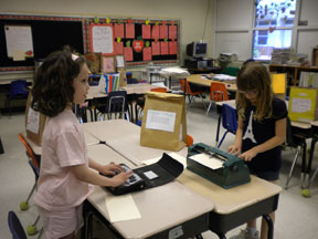 Kendra uses a Braille notetaker while a classmate writes with the Brailler