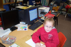 Maegan reads Braille at a desk with a computer behind her