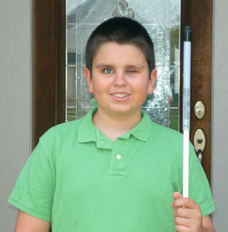 David Thomas stands in front of a house, holding a long white cane