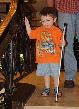 A young boy learns how to descend a staircase using his cane