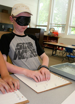 A blind elementary student wearing sleepshades�uses tacks to mark the Braille page he�is reading.