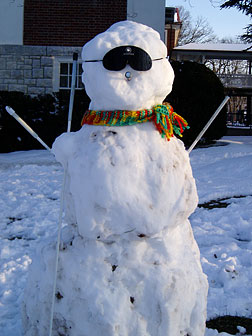 This snowman wears sleepshades and holds his long white cane against his shoulder to get his photo taken.