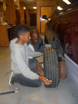 Mentor Garrick Scott shows a student how to change a tire.