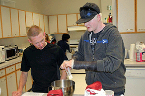 A young man and his mentor drop butter into a mixing bowl.