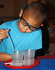 Boy conducts experiment, transferring water from one cup to another with a dropper
