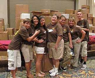 UPS volunteers stand before a mountain of boxes full of Braille books.