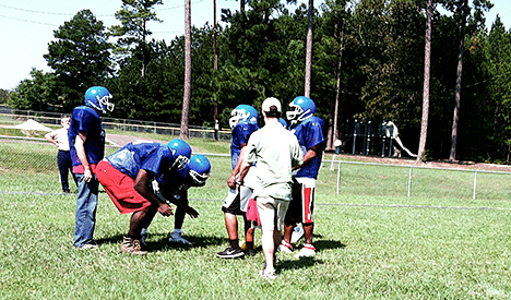 The coach works with six football players while Jerry Whittle looks on.