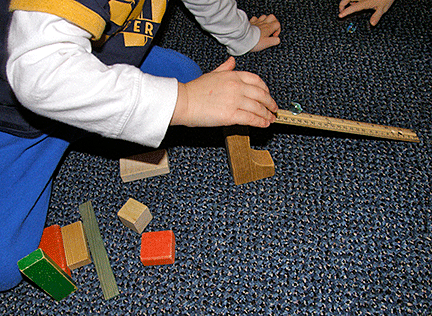 Boy holds ruler as a marble rolls down its inclined plane.